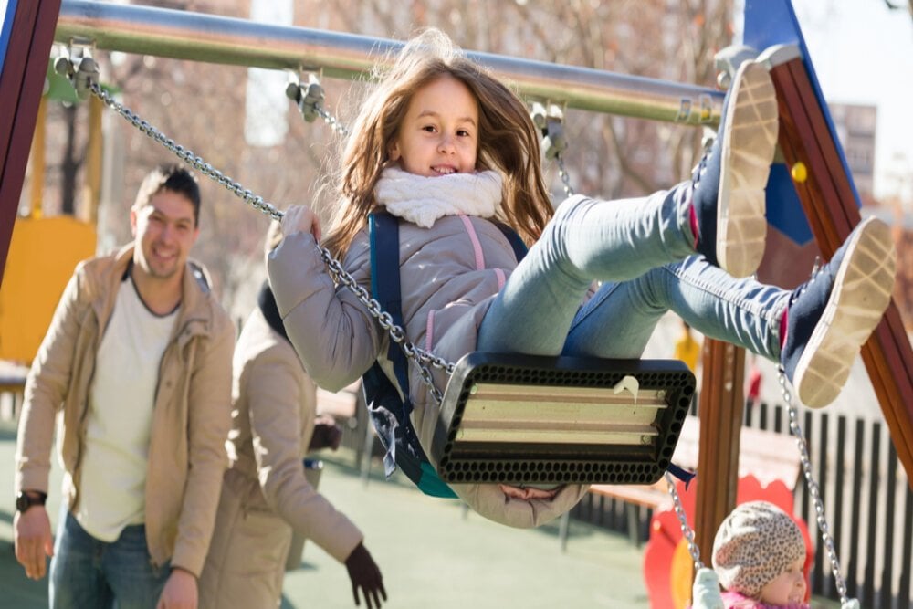 Cheerful,American,Family,With,Two,Girls,Having,Fun,On,Swings
